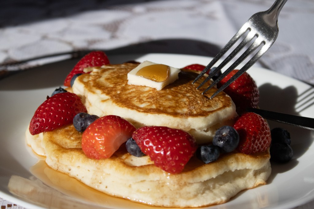 Pancake with fruit, butter, and syrup on it, that is being cut into